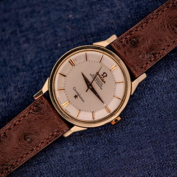 The Omega Constellation Pie-Pan Dial Ref. 167.005 14k Gold Capped watch with a brown leather strap is showcased on a blue fabric background.