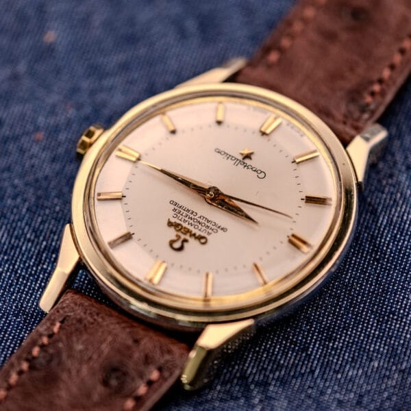 An Omega Constellation Pie-Pan Dial Ref. 167.005 14k gold capped watch with a brown leather strap is displayed elegantly on blue denim fabric.