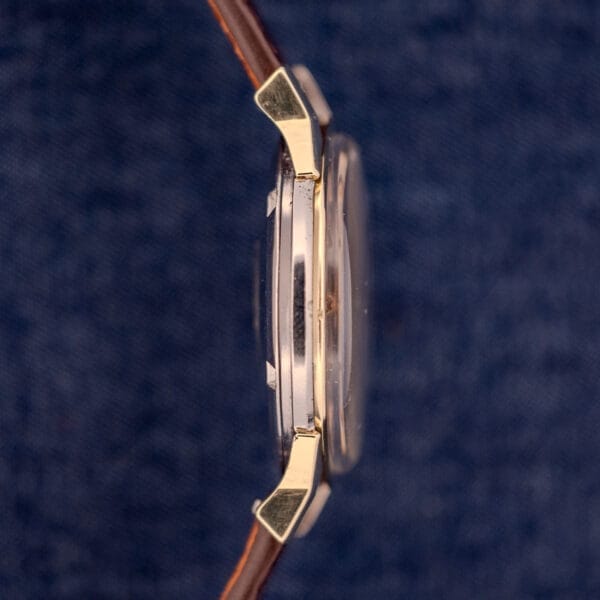 Side view of the Omega Constellation Pie-Pan Dial Ref. 167.005 14k Gold Capped wristwatch with a brown leather strap and signature dial, set against a blue textured background.