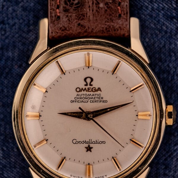 An Omega Constellation Pie-Pan Dial Ref. 167.005 14k Gold Capped wristwatch with a brown leather strap is displayed on a blue fabric background.