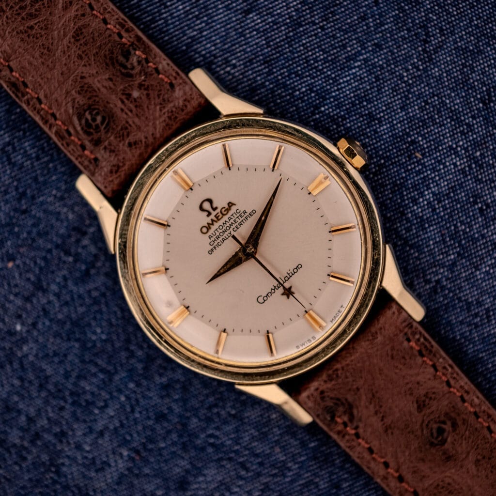 Omega Constellation Pie-Pan Dial Ref. 167.005 with 14k gold capped case, distinctive pie-pan dial, and brown leather strap, elegantly displayed on blue denim fabric.