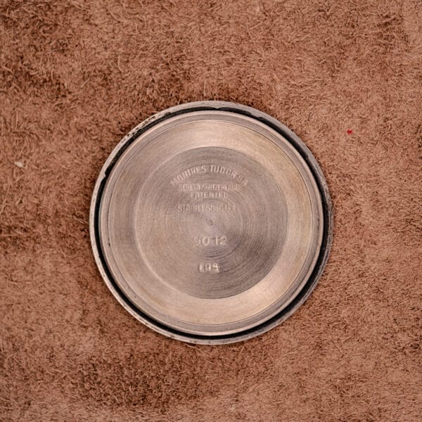 A Tudor Oysterdate Ref. 90120 with a stainless steel sunburst dial is displayed on a textured brown surface.