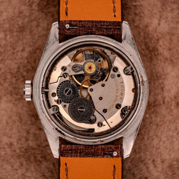 Close-up of a Tudor Oysterdate Ref. 90120 with an exposed mechanical movement, visible gears, sunburst dial, brown leather strap, and classic stainless steel case.
