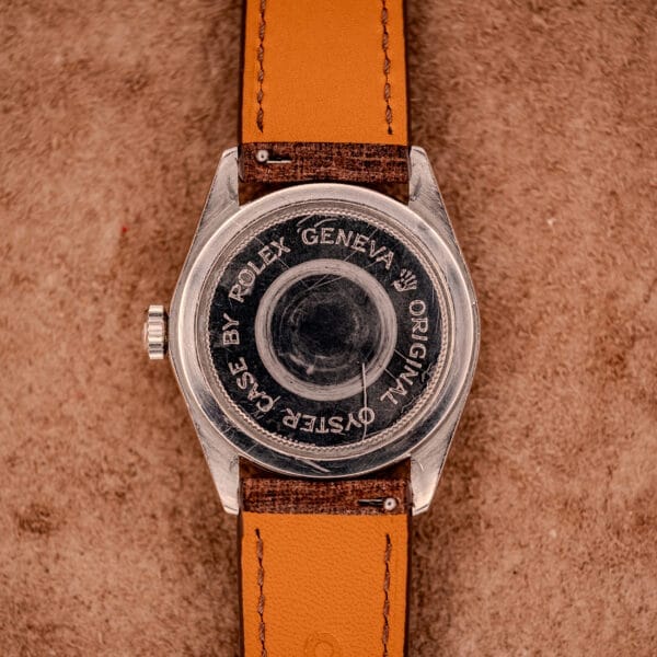 Back view of the Tudor Oysterdate Ref. 90120 Stainless Steel Sunburst Dial watch with a brown leather strap and stainless steel case, displayed on a textured brown surface.