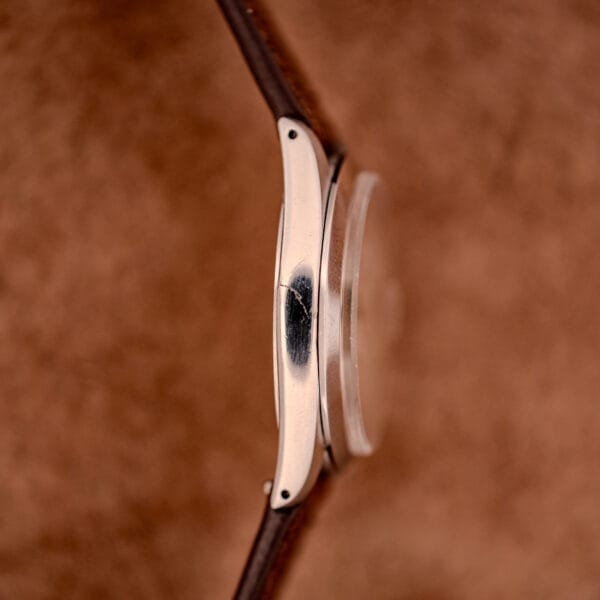 Close-up side view of a Tudor Oysterdate Ref. 90120 Stainless Steel Sunburst Dial watch case, showing a visible scratch on the stainless steel against a brown background.