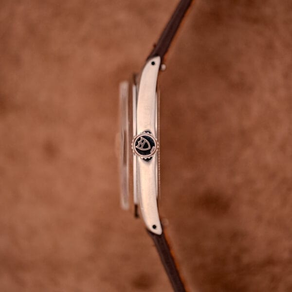 Side view of a Tudor Oysterdate Ref. 90120 Stainless Steel Sunburst Dial wristwatch with a brown leather strap and logo on the crown, set against a brown background.