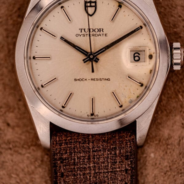 Close-up of a Tudor Oysterdate Ref. 90120 Stainless Steel Sunburst Dial wristwatch featuring a date window and brown textured strap.