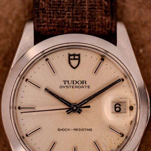 Close-up of a Tudor Oysterdate Ref. 90120 stainless steel watch with a sunburst dial and brown strap, displaying the date as the 6th.