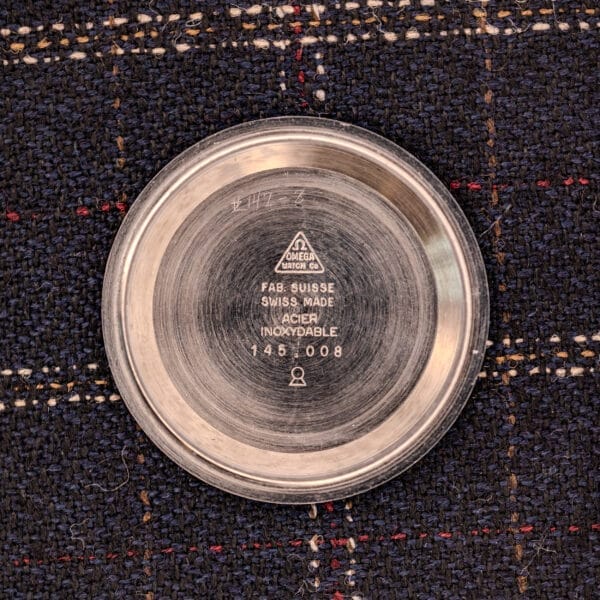 Round metal watch case back with Omega logo and inscriptions referencing the Omega Seamaster Ref. 145.008 Chronostop Regatta Cal. 865, set against a textured dark fabric background.