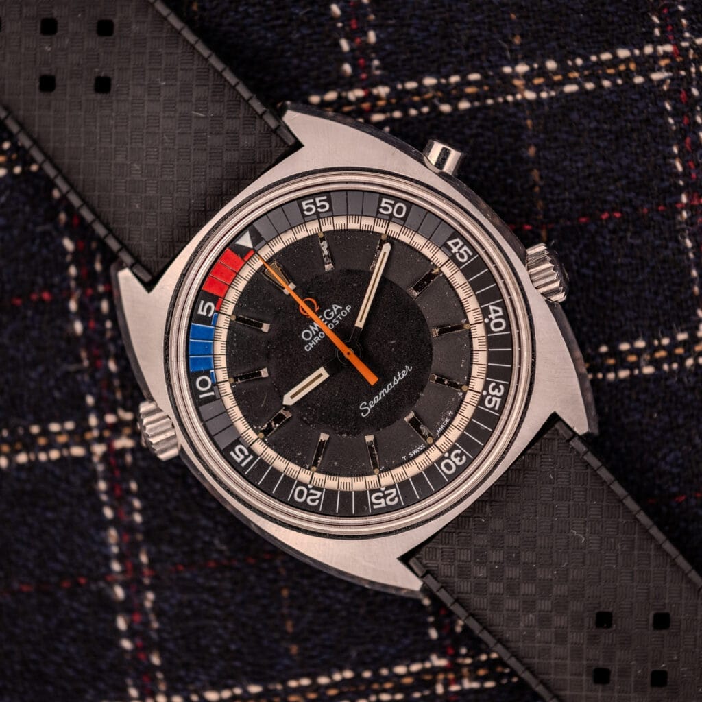 An Omega Seamaster Ref. 145.008 Chronostop Regatta Cal. 865 watch with a black dial and strap, displayed on dark plaid fabric.