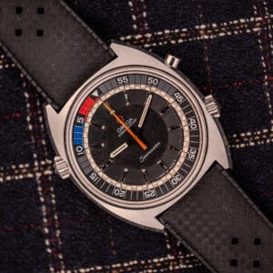 An Omega Seamaster Ref. 145.008 Chronostop Regatta Cal. 865 watch with a black dial and strap, displayed on dark plaid fabric.