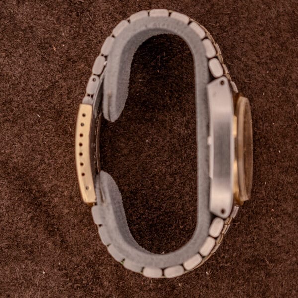 An Omega Constellation Chronometer Ref. 168.045 Day/Date Full Set with a metal band and gold accents, shown on a brown textured surface, viewed from the side.