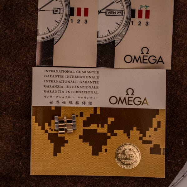 Omega Constellation Chronometer Ref. 168.045 Day/Date Full Set shown with guarantee cards, bracelet links, and a gold seal on a textured brown surface.