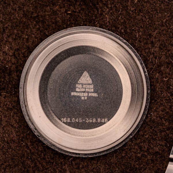 The round stainless steel case back, engraved with 168.045 and other markings, is from an Omega Constellation Chronometer Ref. 168.045 Day/Date Full Set and rests on a dark textured surface.