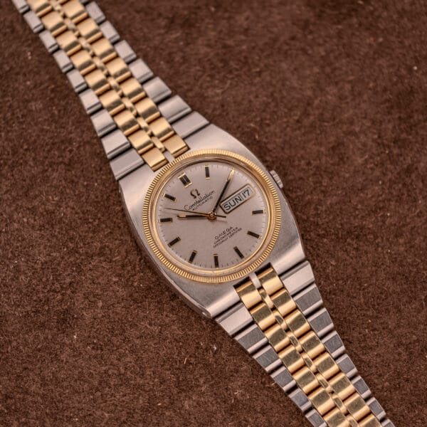 An Omega Constellation Chronometer Ref. 168.045 Day/Date Full Set with a silver dial and two-tone finish, displayed on a brown textured surface.
