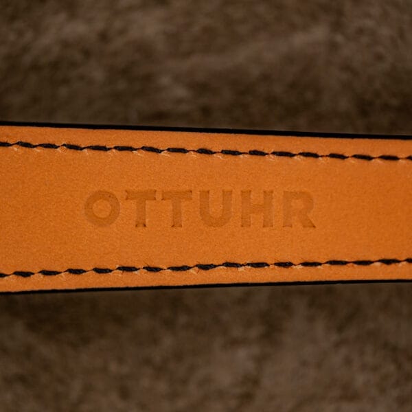 Close-up of a leather strap embossed with OTTUHR, set against a fuzzy brown background—a refined tribute to the Rolex Oyster Perpetual "Big Bubble Back" Ref. 6107 Black Dial and its enduring style.