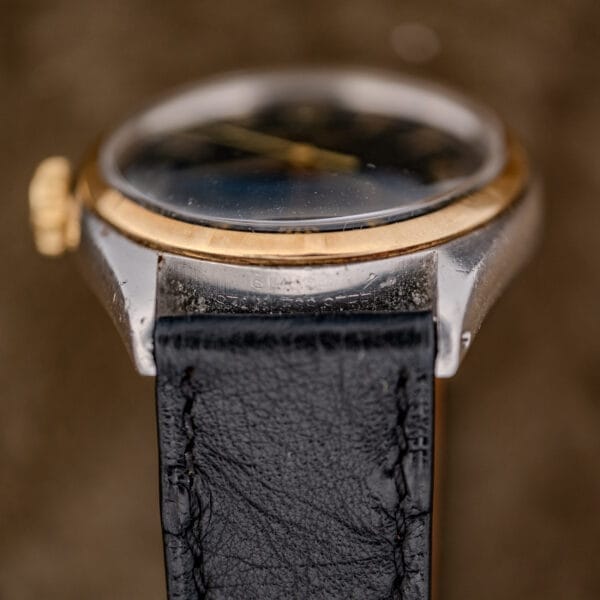 Close-up side view of a Rolex Oyster Perpetual "Big Bubble Back" Ref. 6107 Black Dial, featuring a black leather strap and gold-toned bezel.