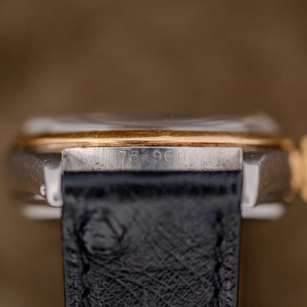 Close-up of a Rolex Oyster Perpetual "Big Bubble Back" Ref. 6107 Black Dial watch with a black leather strap against a brown background.