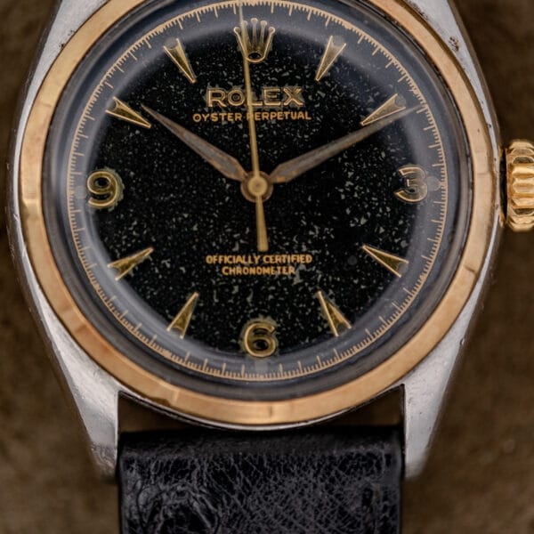 Close-up of a Rolex Oyster Perpetual "Big Bubble Back" Ref. 6107 with a black dial, gold bezel, and black leather strap.