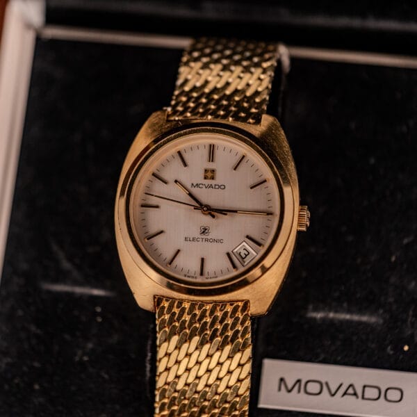 A Movado/Zenith Electronic Tuning Fork Cal ESA 1962 wristwatch with box and papers rests elegantly in a black box, highlighting its refined design.