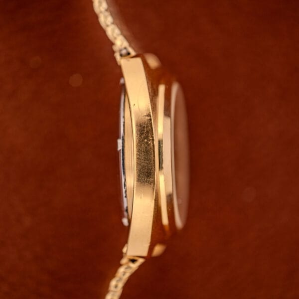 Side view of a gold Movado / Zenith Electronic Tuning Fork Cal ESA 1962 wristwatch with visible scratches on the case, set against a brown background. Box & papers included.