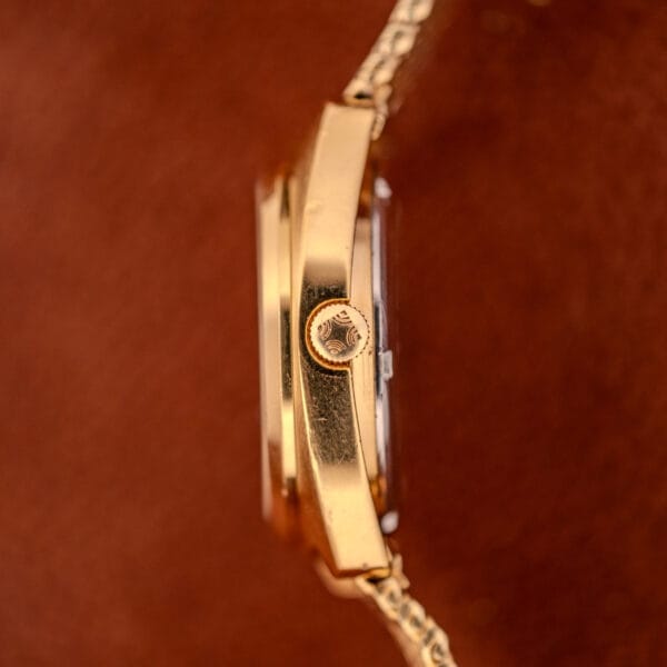 Close-up side view of a Movado / Zenith Electronic Tuning Fork Cal ESA 1962 wristwatch with a crown, shown against a brown background. Box and papers included.