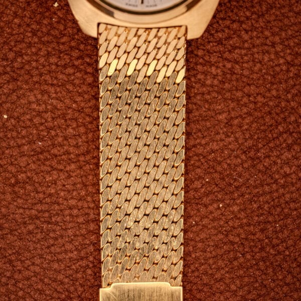 Close-up of the Movado / Zenith Electronic Tuning Fork Cal ESA 1962's gold, woven-pattern wristwatch band on a brown textured background. Includes original box and papers.