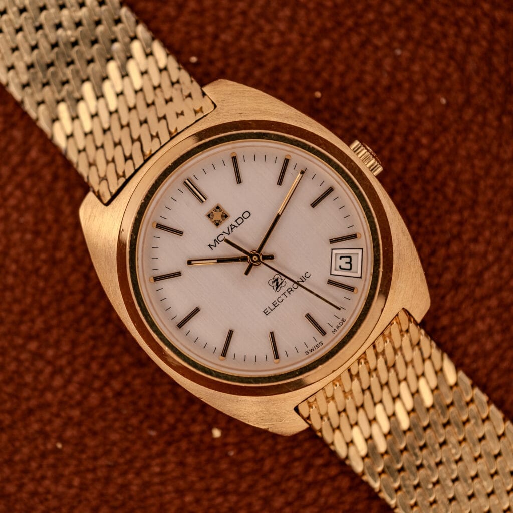 Movado / Zenith Electronic Tuning Fork Cal ESA 1962 wristwatch with a white dial and date display, presented on a brown textured surface, highlights the elegance and precision of this model. Includes box & papers.