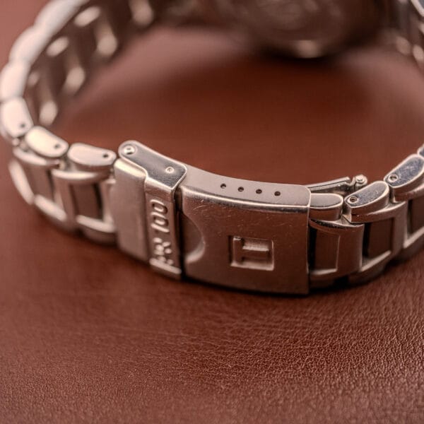 Close-up of the Tissot PR100 Automatic Day/Date P 764 in stainless steel, focusing on its elegant clasp against a brown leather surface and showcasing its refined automatic day/date feature.