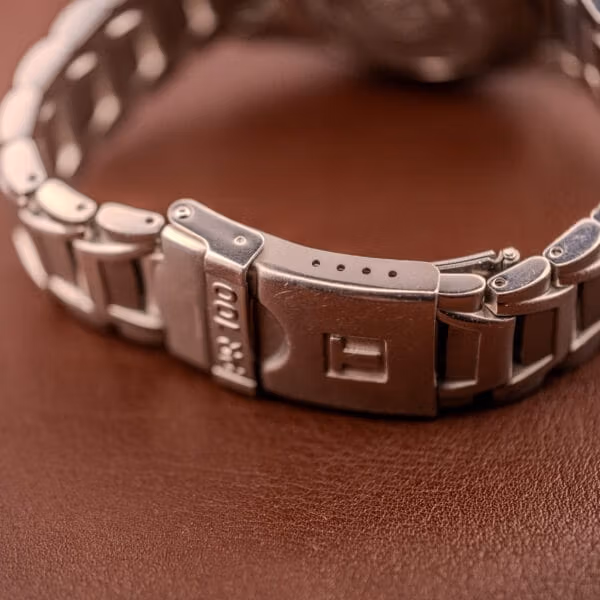 Clasp side of the Tissot PR100 showing additional PR 100 stamping on the bracelet link and the T-logo release button.