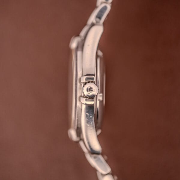 Side view of the Tissot PR100 Automatic Day/Date P 764 in stainless steel, displayed against a soft brown background.