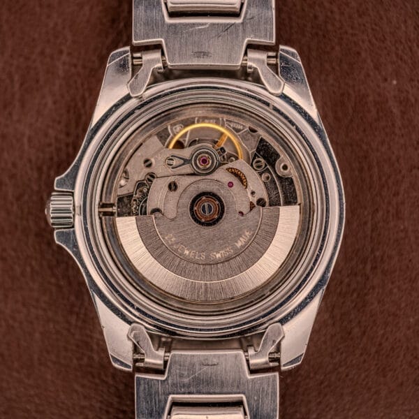 Close-up of the Tissot PR100 Automatic Day/Date P 764 movement, showcasing visible gears and components inside its stainless steel case.