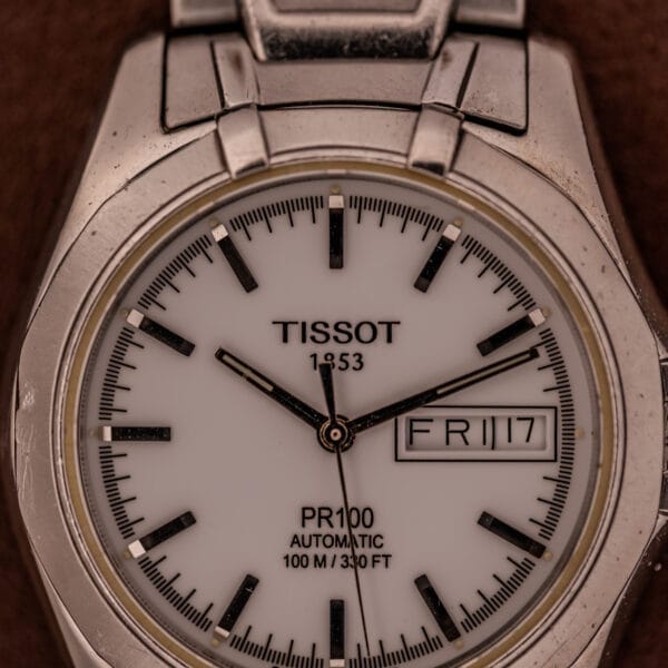 Close-up of the Tissot PR100 Automatic Day/Date P 764 in stainless steel, featuring an elegant white dial with the day "FRI" and date "17" displayed.
