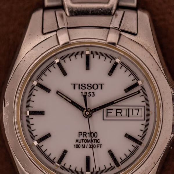 Straight-on dial of the Tissot PR100 Automatic Day/Date with TISSOT 1853 at twelve and the day-date complication framed at three.