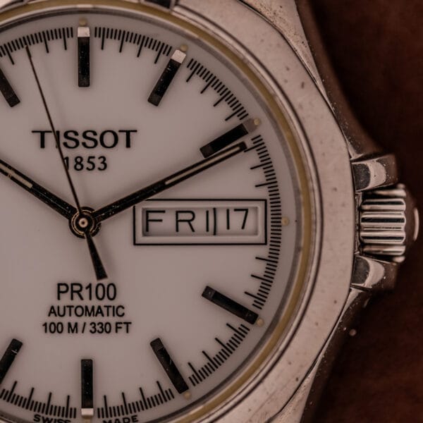 Close-up of a Tissot PR100 Automatic Day/Date P 764 in Stainless Steel, displaying FRI and 17 on its white dial.