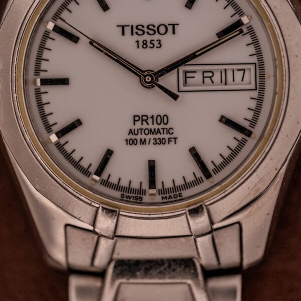 Close-up of a Tissot PR100 Automatic Day/Date P 764 in stainless steel, displaying the time at 10:08 and the date as Friday the 17th.