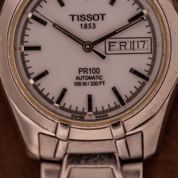 Dial close-up of the Tissot PR100 Automatic with applied polished batons, TISSOT 1853 signature, and FRI 17 in the day-date window.