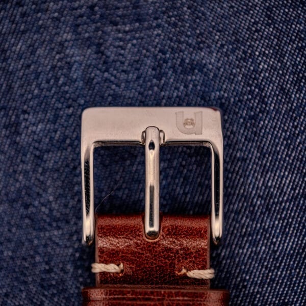 Close-up of a silver belt buckle on a brown leather strap over blue denim, exuding the refined elegance of the Longines Square 10k Gold Filled Case Waffle Dial Cal. 25Z.