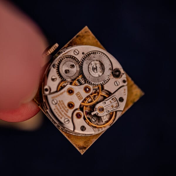 Close-up of intricate gears and components inside a Longines Square 10k Gold Filled Case Waffle Dial Cal. 25Z mechanical watch, set against a dark background.