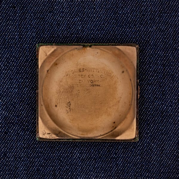 A Longines Square 10k Gold Filled Case Waffle Dial Cal. 25Z watch case back with engraved text rests on dark blue textured fabric, showcasing its timeless elegance and classic gold-filled design.