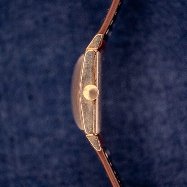 Side view of a Longines Square 10k gold filled case watch with waffle dial Cal. 25Z and brown leather strap, set against a blue fabric background.