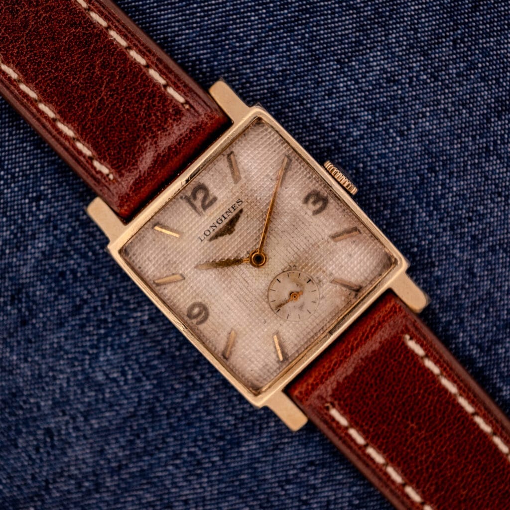Longines Square 10k Gold Filled Case Waffle Dial Cal. 25Z watch with a brown leather strap, classic waffle dial, and vintage style, shown on blue denim fabric.