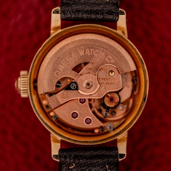 Close-up of the Omega Ladymatic Sunburst Dial Ref. W 5294 Cal. 680, featuring its exposed mechanical movement, gold case, and black leather strap.