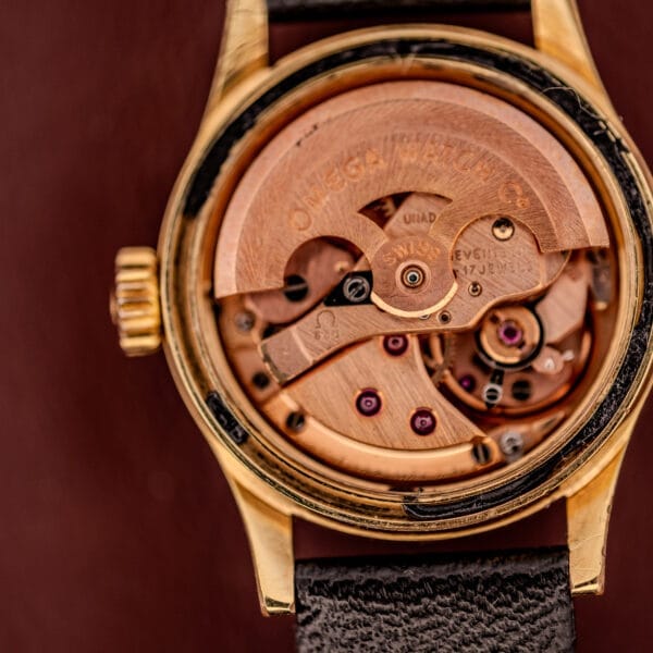 Close-up of an Omega Ladymatic Sunburst Dial Ref. MD 566.021, showcasing its exposed Cal. 680 mechanical movement in a gold case with a leather strap.