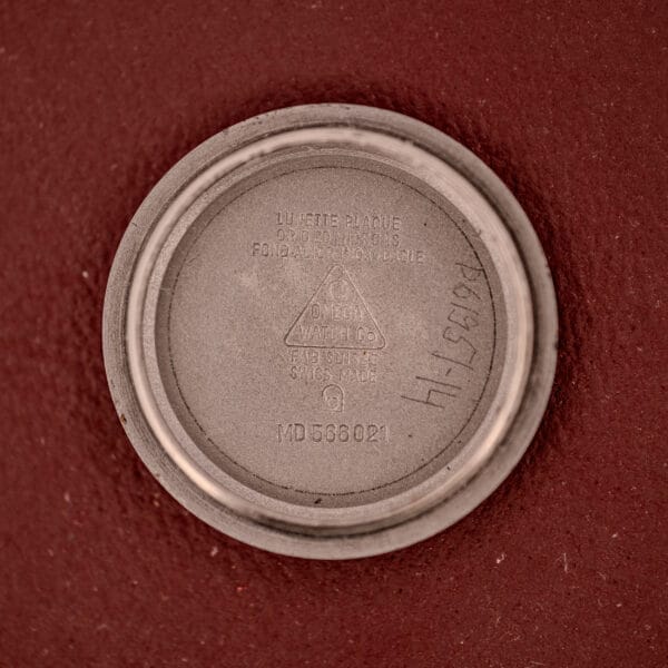 The round metal case back engraved with the Omega logo and reference numbers rests on a red textured surface, belonging to the Omega Ladymatic Sunburst Dial Ref. MD 566.021 Cal. 680.