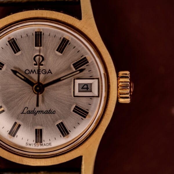 Close-up of the Omega Ladymatic Sunburst Dial Ref. MD 566.021 Cal. 680 gold wristwatch, featuring a sunburst dial with date display and part of its elegant watch face.