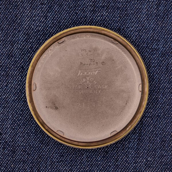 The round metal case back of the Tissot Automatic Bumper Black Dial & Gold Filled Case Cal. 28.5T, engraved with markings, rests on blue textured fabric.