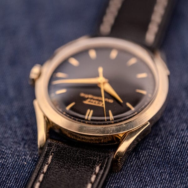 A Tissot Automatic Bumper Black Dial & Gold Filled Case Cal. 28.5T wristwatch with a black dial and gold filled case, paired with a black leather strap, resting on blue fabric.