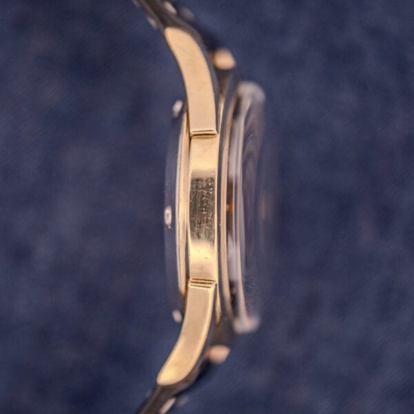 Side view of a Tissot Automatic Bumper with black dial and gold filled case Cal. 28.5T, set against a blue textured background.