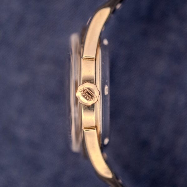 Side view of the Tissot Automatic Bumper Black Dial & Gold Filled Case Cal. 28.5T, set against a textured blue background.